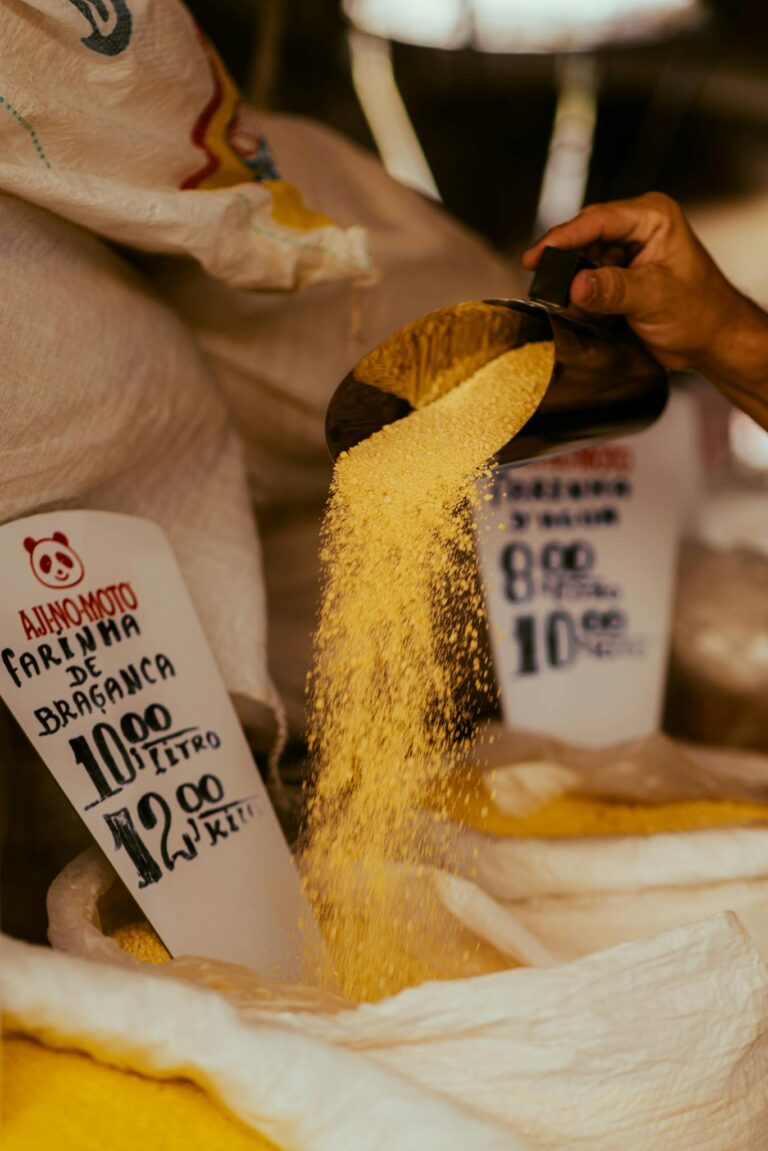 Close-up of hand pouring Bragança flour from scoop in a market with price tags visible.